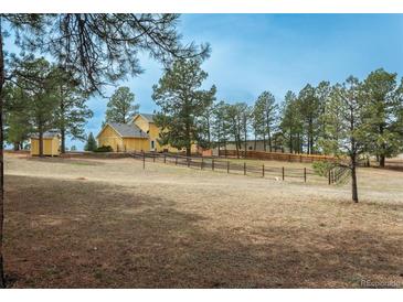 Wide shot of home's yellow exterior, surrounding trees, and large front yard enclosed by wood fence at 37677 Sable Ridge Rd, Elizabeth, CO 80107