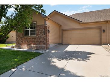 Tan home featuring a two-car garage, brick accents, and well-maintained landscaping at 16141 W 64Th Way, Arvada, CO 80007