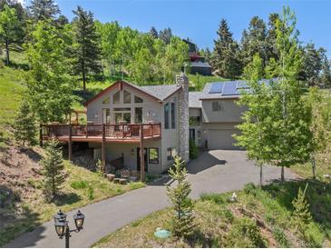 Charming multi-level home with stone chimney, large deck, and solar panels surrounded by lush trees at 32209 Blue Springs Dr, Evergreen, CO 80439