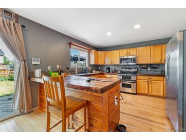 This kitchen features wood cabinets, stainless steel appliances, and a rustic wood breakfast bar at 1086 Mockingbird St, Brighton, CO 80601