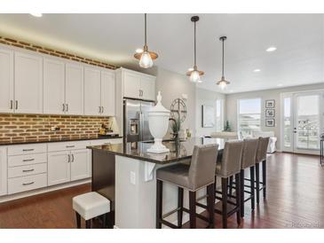 Modern kitchen features an island with seating, granite countertops, stainless appliances, and a brick backsplash at 3698 Penang Dr, Castle Rock, CO 80109