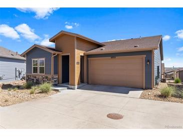 Charming exterior view of home with a two-car garage, stone accents, and blue and tan siding at 10723 N Montane Dr, Broomfield, CO 80021