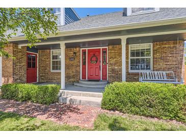 Charming brick home features a covered front porch and bright red front door with a decorative wreath at 9929 W Fairview Ave, Littleton, CO 80127