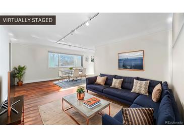 A virtually staged living room featuring a blue couch, dining table, and wood floors at 1175 N Emerson St # 308, Denver, CO 80218