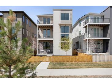 Modern three-story home featuring private balconies, stone accents, and a wooden fence, enhancing curb appeal at 21418 E 61St Dr, Aurora, CO 80019