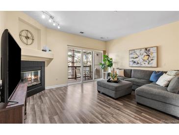 Bright living room features a cozy fireplace, gray sectional sofa, and sliding glass doors to the balcony at 7459 S Alkire St # 202, Littleton, CO 80127