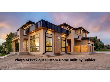 Modern exterior with tan stucco, dark trim, stone accents, outdoor lighting, and metal and wood railings at 1055 Greens Pl, Erie, CO 80516