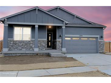 Charming home featuring stone accents, a covered entryway, and a gray garage door at dusk at 17170 E 90Th Pl, Commerce City, CO 80022
