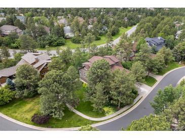 Aerial view of a wooded neighborhood with a brown two story house featuring mature trees and lush landscaping at 1122 Forest Trails Dr, Castle Pines, CO 80108