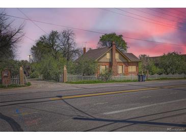 Charming brick home with a white picket fence and mature trees under a beautiful sky at 5475 W 1St Ave, Lakewood, CO 80226