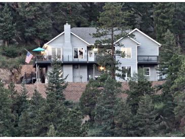 Charming gray two-story home nestled on a hill surrounded by lush trees and multiple decks at 83 Wilderness Cornerstone Rd, Evergreen, CO 80439