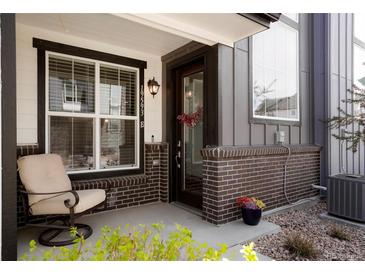 Inviting front porch features a cozy chair, brick accents, and decorative floral arrangements at 19593 W 93Rd Ln # E, Arvada, CO 80007