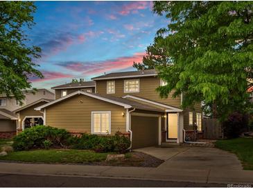 Charming two-story home featuring an attached garage, mature trees, and colorful bushes, captured during a vibrant sunset at 12599 Elm St, Thornton, CO 80241