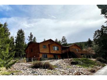 Stunning two-story home with a wooden exterior, charming deck, and lush, mature trees at 29825 Kennedy Gulch Rd, Conifer, CO 80433