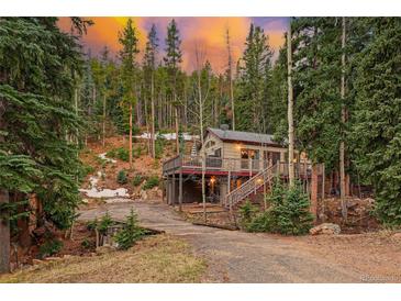 Charming mountain home with wrap-around deck nestled among tall evergreen trees at sunset at 34788 Forest Estates Rd, Evergreen, CO 80439