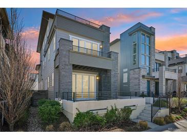 Modern two-story home features gray siding, stone accents, metal railings, and an expansive front porch at 9006 E 60Th Ave, Denver, CO 80238