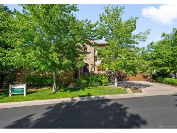 Stone home featuring mature trees, a lush lawn, and a driveway leading to an attached two-car garage at 9151 E Harvard Ave, Denver, CO 80231