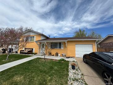 Charming yellow home featuring a well-manicured lawn and a driveway with a black car at 14595 Robins Dr, Denver, CO 80239