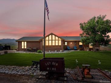 Charming brick home featuring a well-maintained lawn, mature tree, and unique mining cart decor at 16535 W 79Th Dr, Arvada, CO 80007