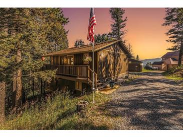 Charming home featuring a front porch, wood siding, and a gravel driveway surrounded by lush trees at 31084 Kings Valley Dr, Conifer, CO 80433