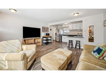 Open living room featuring wood floors, a television, and a stainless steel refrigerator in an adjacent kitchen at 1734 Kingston St, Aurora, CO 80010