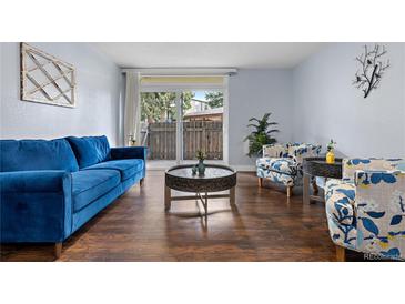 Bright living room with wood floors, blue sofa, and chairs; view to outdoor space through sliding glass door at 2281 Vaughn # 104A, Aurora, CO 80014