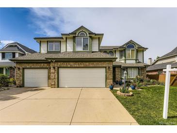 Two story brick home with three car garage, well manicured lawn and colorful flower beds at 5426 S Jasper Way, Centennial, CO 80015