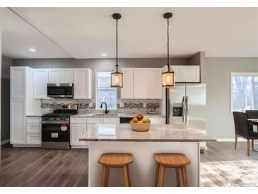 Modern kitchen with white cabinets, stainless steel appliances, granite countertops, and stylish pendant lighting over an island with seating at 530 Hickory St, Hudson, CO 80642