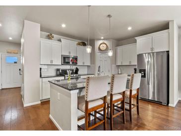 Bright kitchen features an island with seating, granite countertops, stainless steel appliances, and white cabinets at 9235 Quintero St, Commerce City, CO 80022