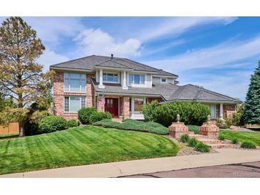 Charming brick home featuring a manicured lawn, brick stairs and pillars, and a red front door at 15573 E Prentice Ln, Centennial, CO 80015