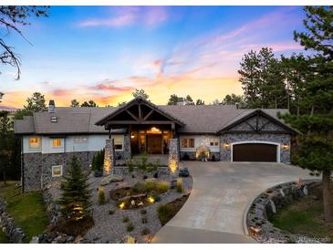 Stunning stone home with a covered entrance, lush landscaping, and a circular driveway at sunset at 4491 Shoshone Dr, Larkspur, CO 80118