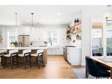 Bright, open kitchen with stainless steel appliances, white cabinets, island with seating and floating shelves at 8357 W 68Th Ln, Arvada, CO 80004