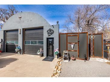 Unique Quonset-style home featuring an arched roof, garage doors, artistic details, and decorative fencing at 410 Goodrich Ave, Platteville, CO 80651