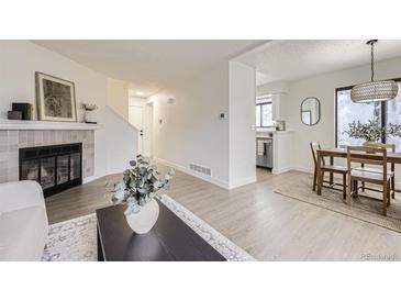 Inviting living room with fireplace, dining area, and adjacent kitchen featuring modern, light wood-style flooring at 1700 W 102Nd Ave, Thornton, CO 80260