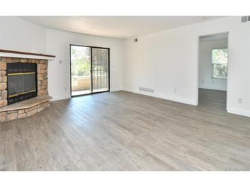 Bright living room features a stone fireplace, modern flooring, and a sliding glass door to outdoor space at 12024 W Cross Dr # 106, Littleton, CO 80127