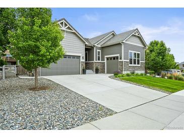 A home with great curb appeal has a well-maintained lawn and a convenient two-car attached garage with stone accents at 16256 Ute Peak Way, Broomfield, CO 80023