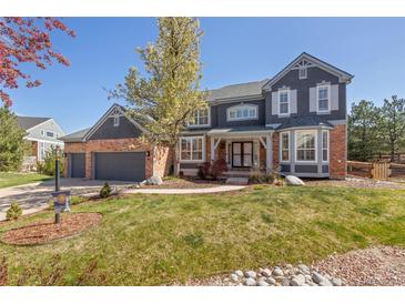 Elegant two-story home with brick and siding exterior, mature landscaping, and an attached three-car garage at 404 Yarrow Pl, Castle Pines, CO 80108