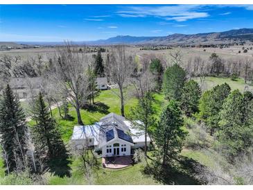 Stunning aerial view of a white home with solar panels, green lawn, mature trees, and mountain views at 9445 Lykins Pl, Longmont, CO 80503