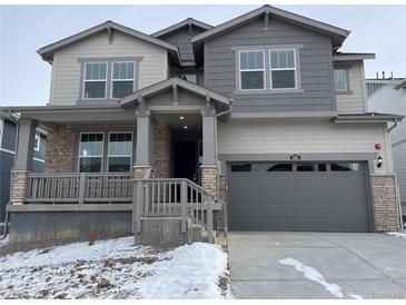 Two-story home featuring varied gray siding, stone accents, covered front porch, and two-car garage, offering classic curb appeal at 585 Twilight St, Erie, CO 80516