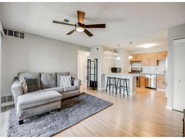 Bright living room featuring modern ceiling fan, plush gray sofa, and open access to the kitchen area at 2575 S Syracuse Way # K201, Denver, CO 80231