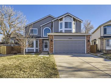 Charming two-story home with gray siding, brick accents, manicured lawn, and attached two-car garage at 13322 Marion St, Thornton, CO 80241