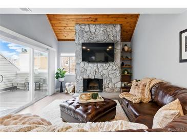Cozy living room featuring a stone fireplace, wood ceiling, leather furniture, and sliding door access to the outside at 2658 S Xanadu Way # B, Aurora, CO 80014