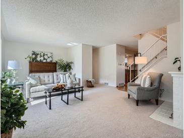 Bright living room features plush carpeting, a stylish sofa, and modern decor with a fireplace and staircase at 9057 E Oxford Dr, Denver, CO 80237