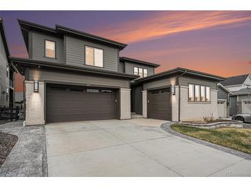 Modern home boasting a three car garage, sleek gray siding, and decorative stone accents against a vibrant sunset sky at 6429 Stable View St, Castle Pines, CO 80108