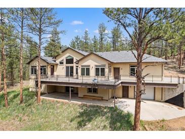 Spacious stucco home featuring an expansive deck with metal railings, surrounded by a lush green lawn and mature trees at 510 Hill Dr, Sedalia, CO 80135