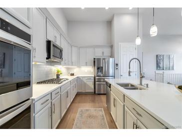 This kitchen features white cabinetry, stainless steel appliances, and a large island with a sink at 1588 Blackwood Ct, Erie, CO 80516