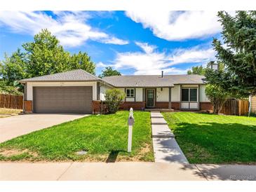 Charming ranch-style home with a well-manicured lawn, mature trees, and a two-car garage on a sunny day at 17177 E Milan Cir, Aurora, CO 80013