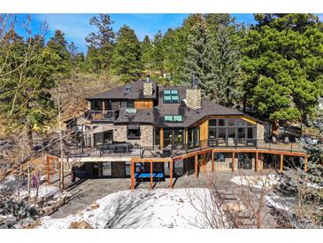 Stunning multi-level stone house with a large deck nestled in a wooded landscape, providing serene outdoor living spaces at 4398 Cameyo Rd, Indian Hills, CO 80454