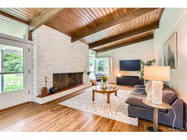 Bright living room featuring a brick fireplace, wood ceiling beams, hardwood floors, and a comfortable seating area at 845 Everett St, Lakewood, CO 80215