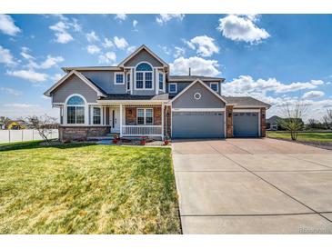 Charming two-story home featuring a welcoming front porch and three-car garage on a sunny day at 16680 Stroilway St, Hudson, CO 80642